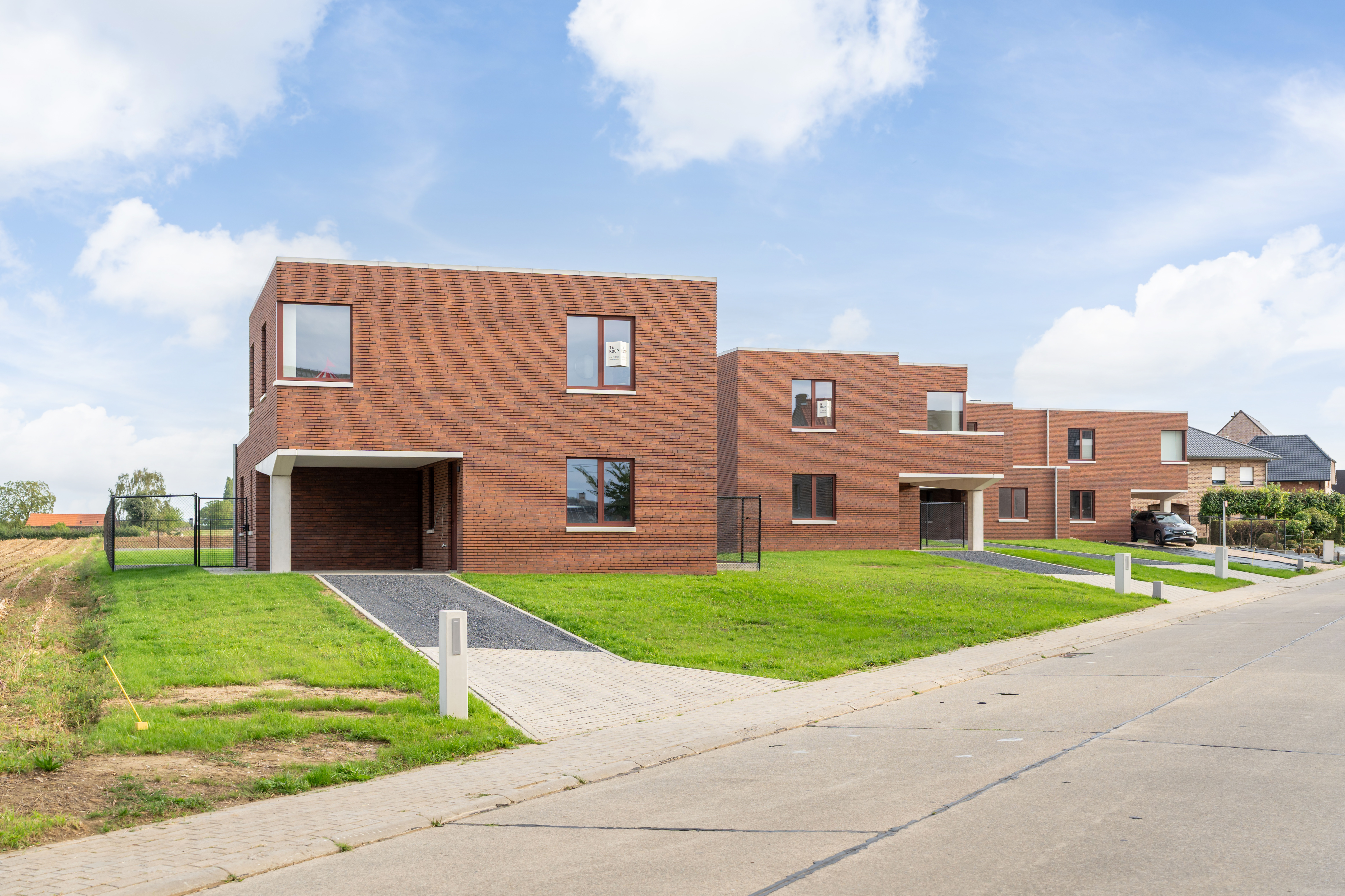 De vrijstaande woning vanaf de straat, met oprit, carport en akker ernaast