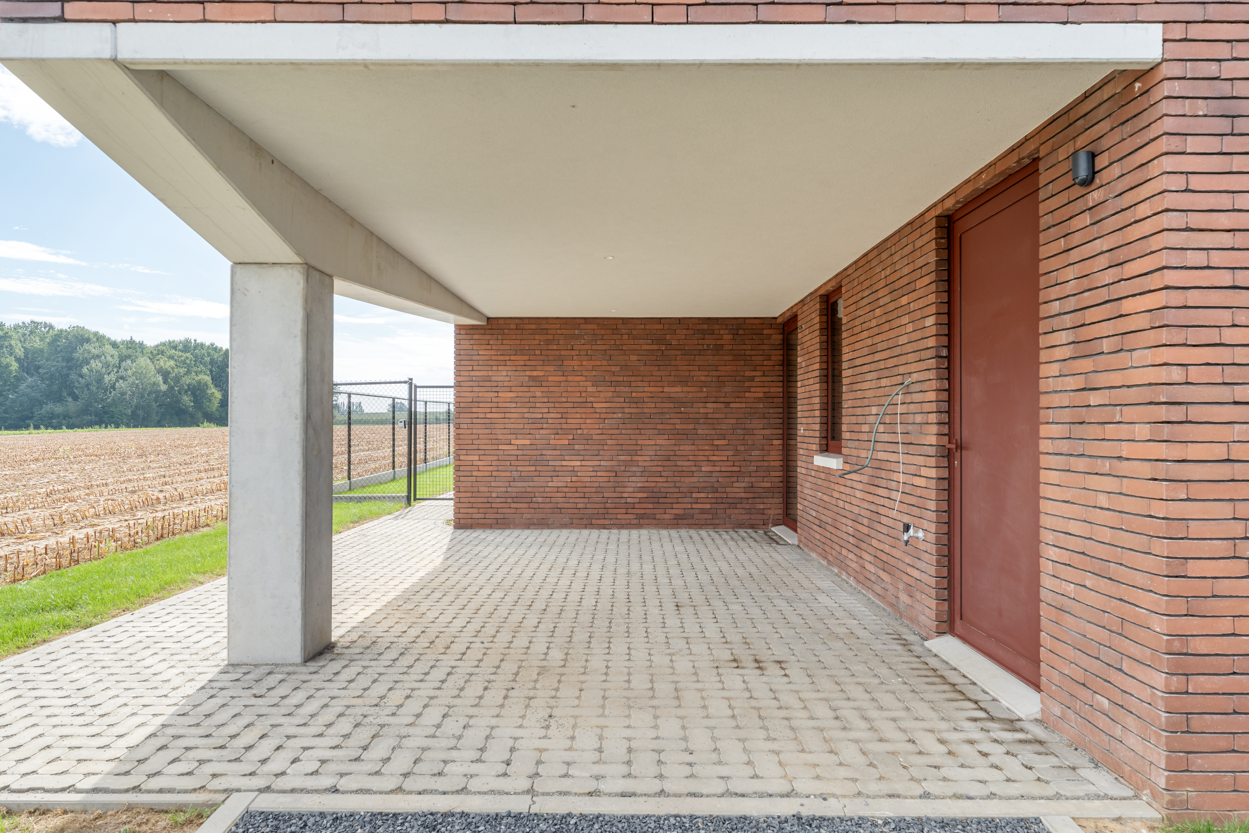 Carport in zichtbeton en vormbaksteen met doorkijk naar de velden